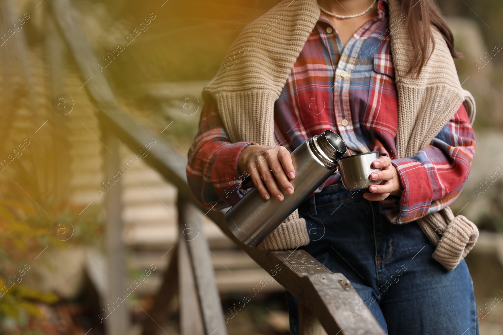 Photo of Woman pouring hot drink from metallic thermos into cup lid outdoors, closeup. Space for text