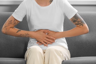 Photo of Young woman suffering from menstrual pain on sofa indoors, closeup