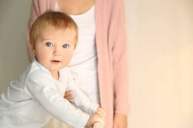 Photo of Cute little baby and mother near light wall indoors