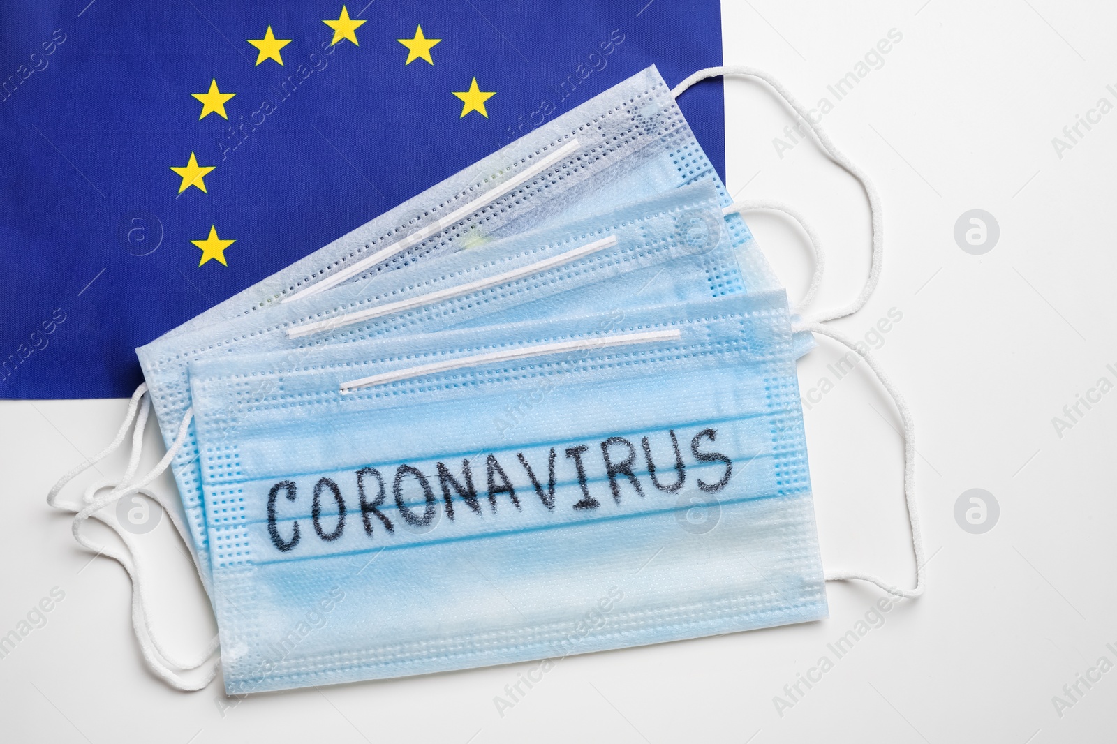 Photo of Protective masks and European Union flag on white background, flat lay. Coronavirus outbreak