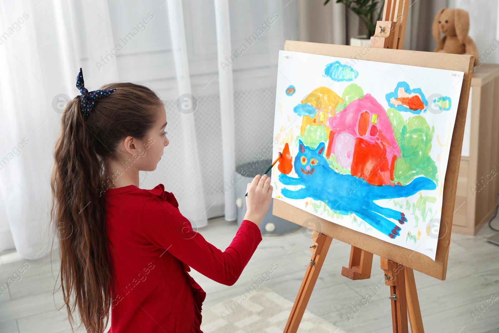 Photo of Little child painting picture using easel at home