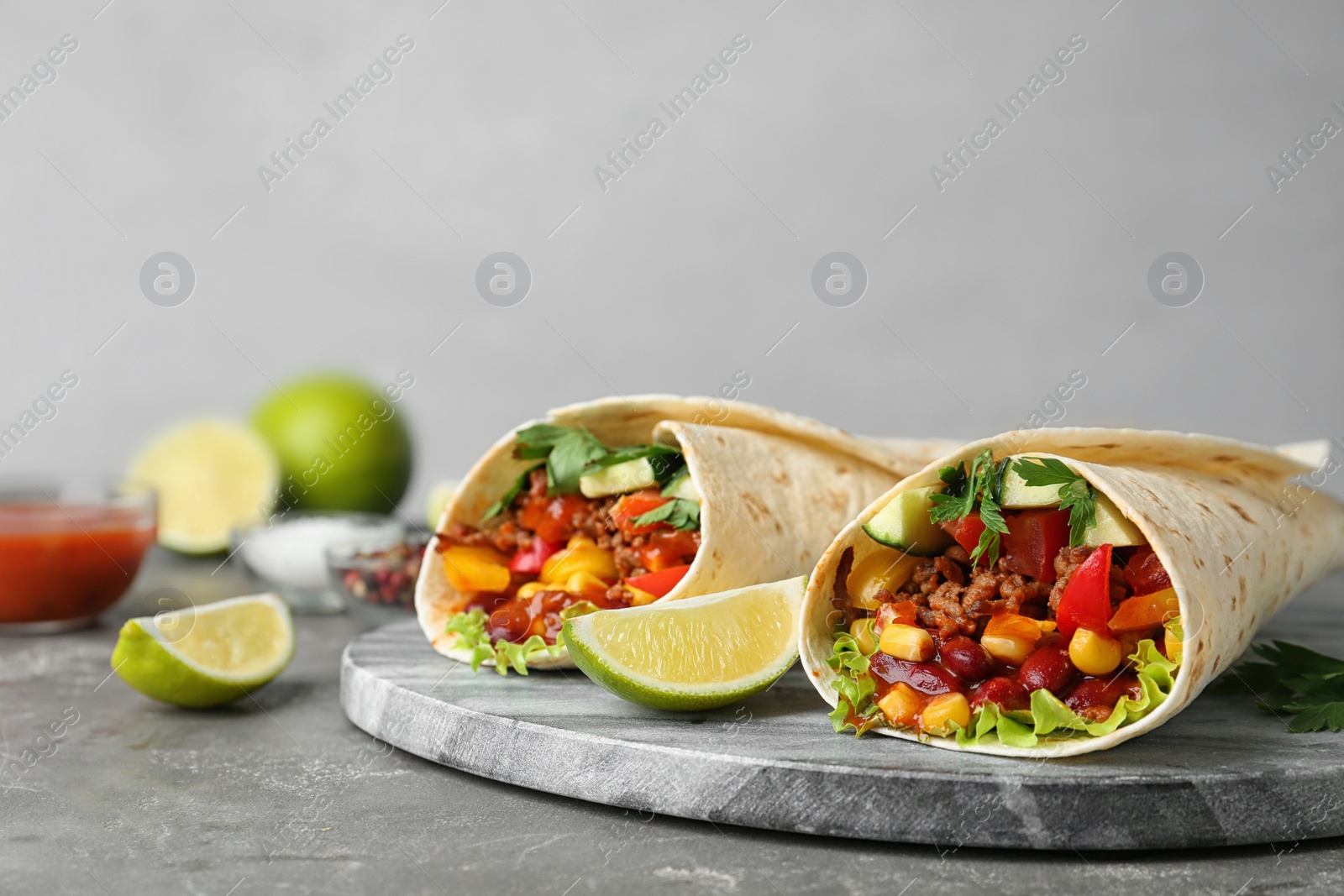 Photo of Board with delicious meat tortilla wraps on grey table