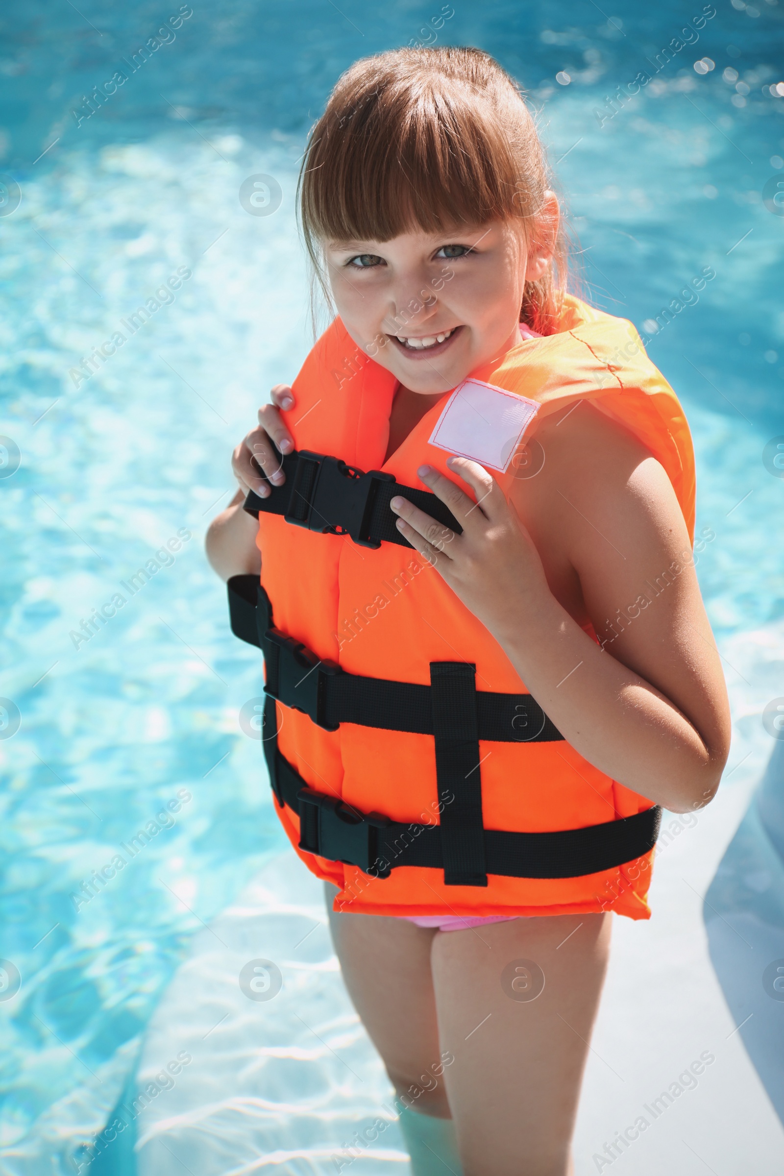 Photo of Little girl wearing orange life vest in outdoor swimming pool