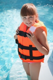 Little girl wearing orange life vest in outdoor swimming pool