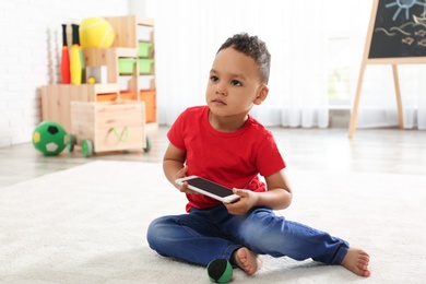 Photo of Cute little African-American child playing on mobile phone in kindergarten. Indoor activity