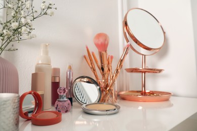 Photo of Mirror and makeup products on white dressing table near wall
