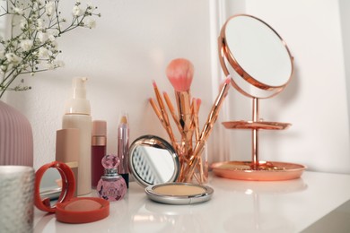 Mirror and makeup products on white dressing table near wall