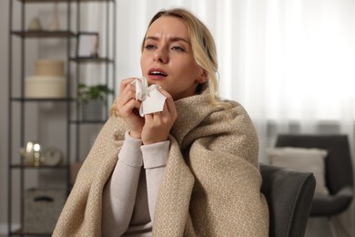 Photo of Sick woman wrapped in blanket with tissue sneezing at home. Cold symptoms