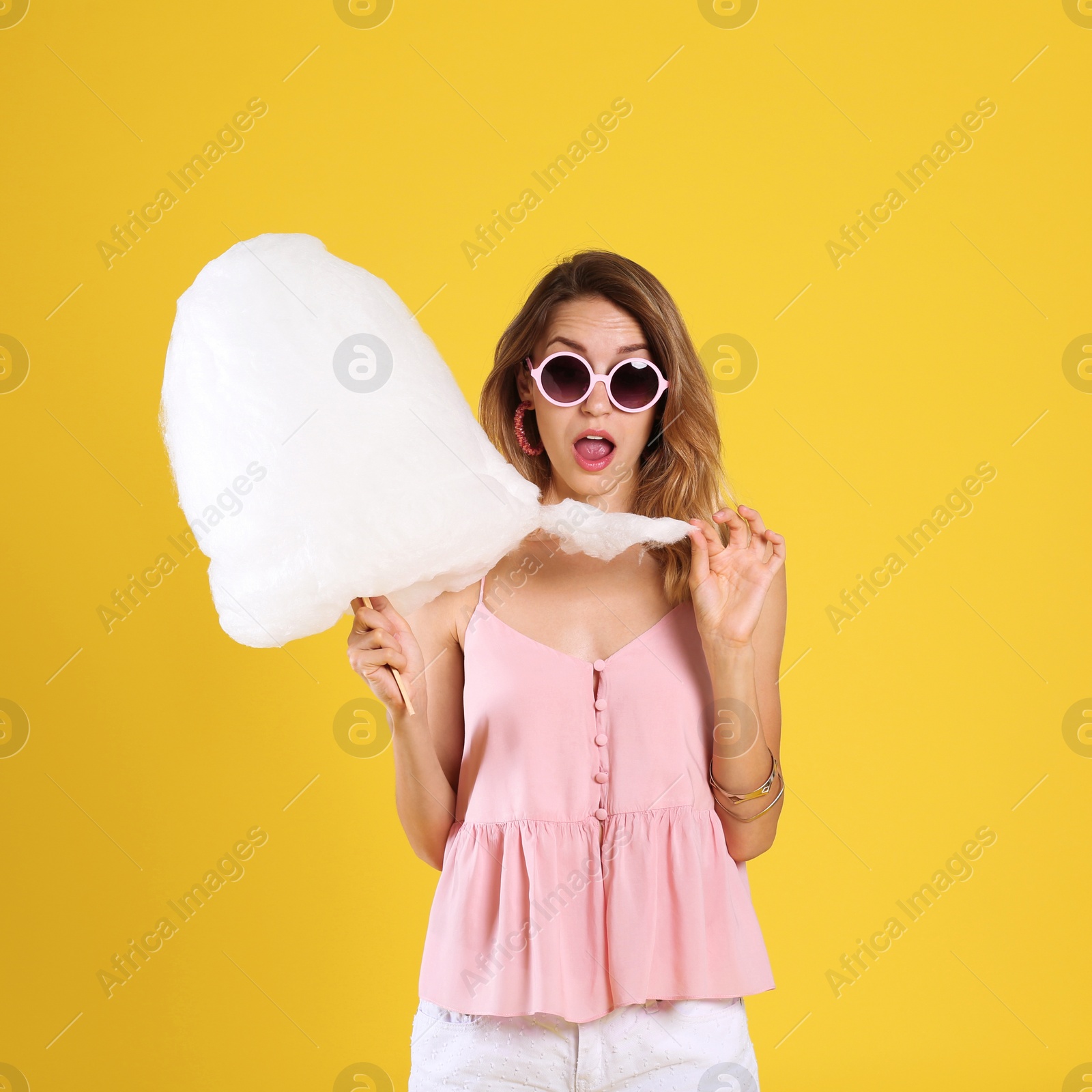 Photo of Emotional young woman with cotton candy on yellow background