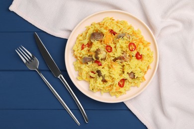 Delicious pilaf with meat served on blue wooden table, flat lay