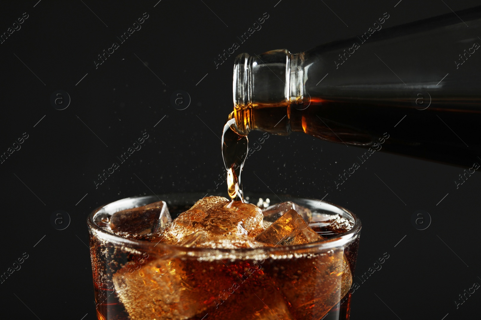 Photo of Pouring refreshing soda water from bottle into glass on black background, closeup