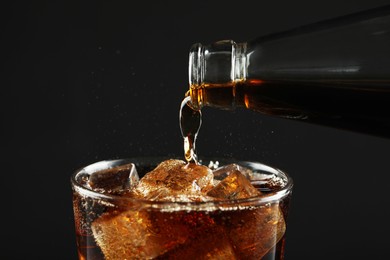 Photo of Pouring refreshing soda water from bottle into glass on black background, closeup