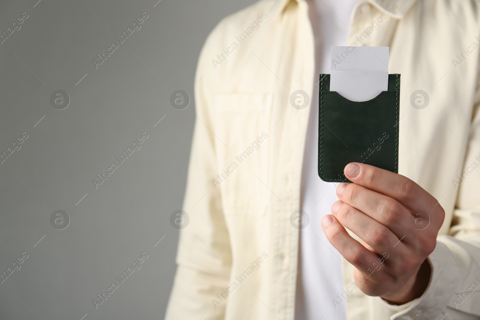 Photo of Man holding leather business card holder with cards on grey background, closeup. Space for text