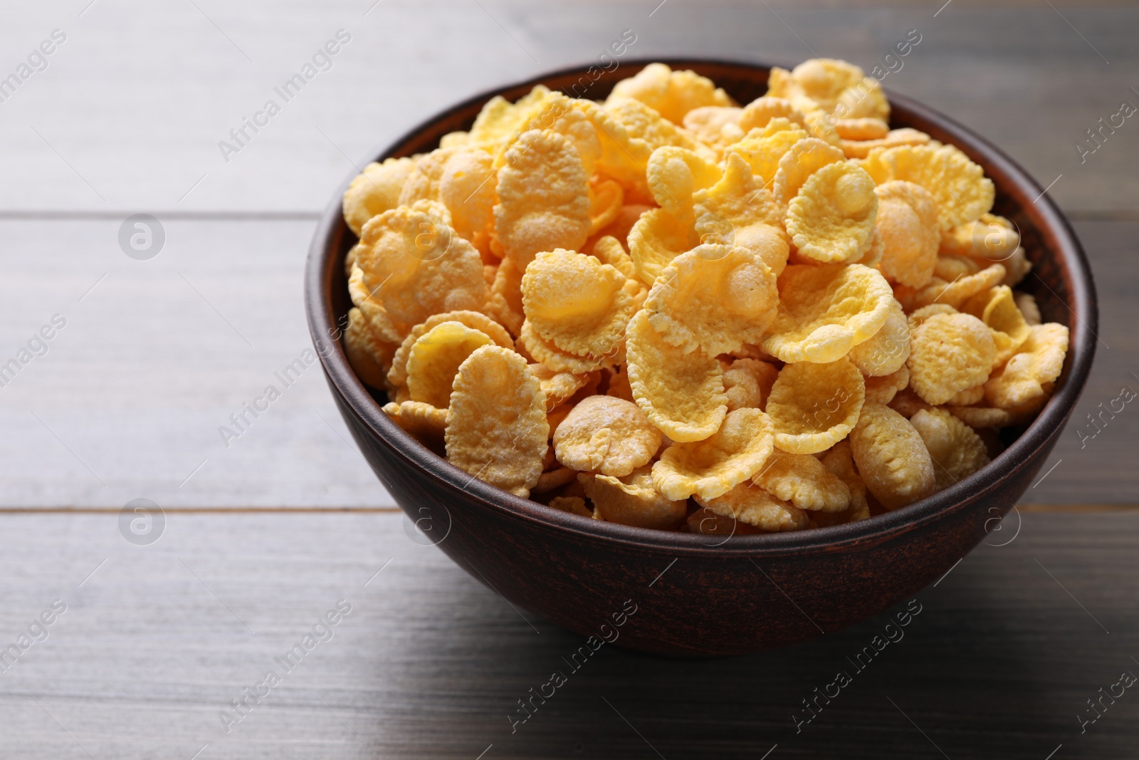 Photo of Bowl of tasty crispy corn flakes on wooden table, closeup