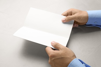 Photo of Young man holding blank brochure at grey table, closeup. Mock up for design