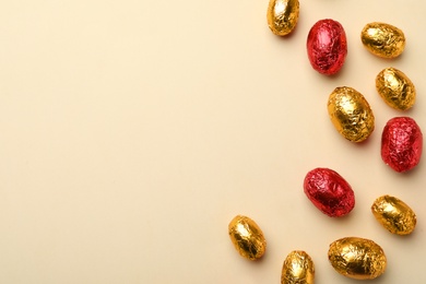 Photo of Chocolate eggs wrapped in red and golden foil on beige background, flat lay. Space for text