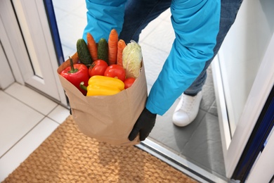 Photo of Courier holding paper bag with food in doorway, closeup. Delivery service during quarantine due to Covid-19 outbreak