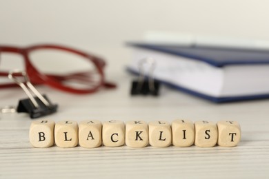 Photo of Cubes with word Blacklist and office stationery on white wooden desk, closeup