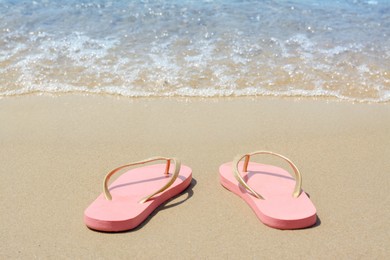 Stylish pink flip flops on sandy beach near sea