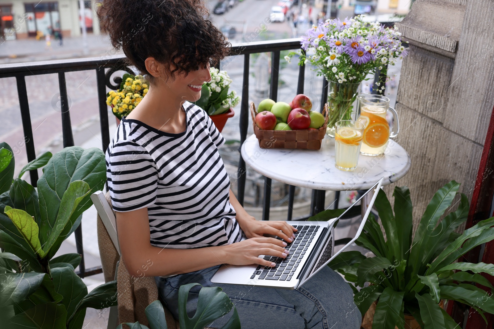 Photo of Beautiful young woman using laptop on balcony with green houseplants