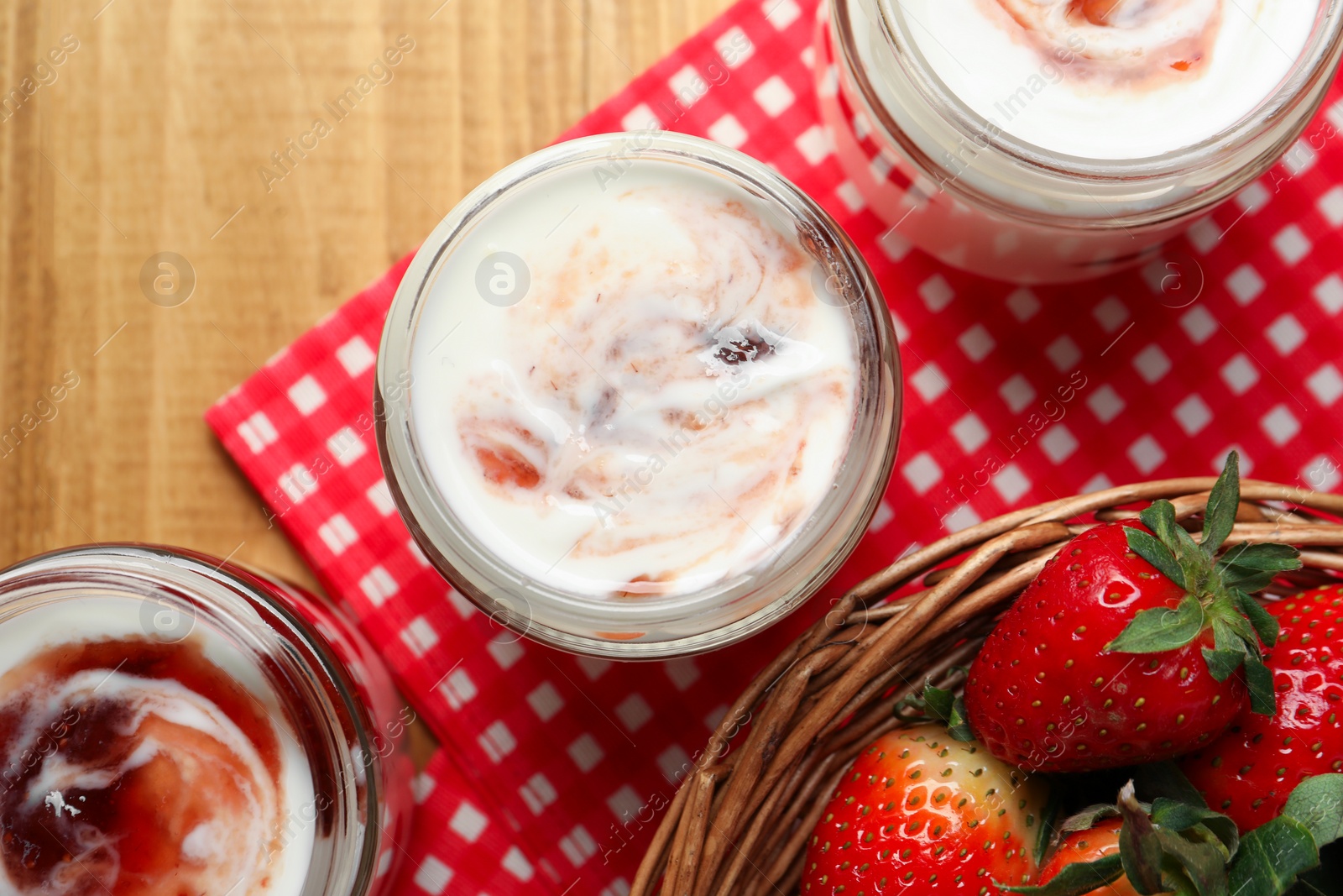 Photo of Tasty yoghurt with jam and strawberries on wooden table, top view