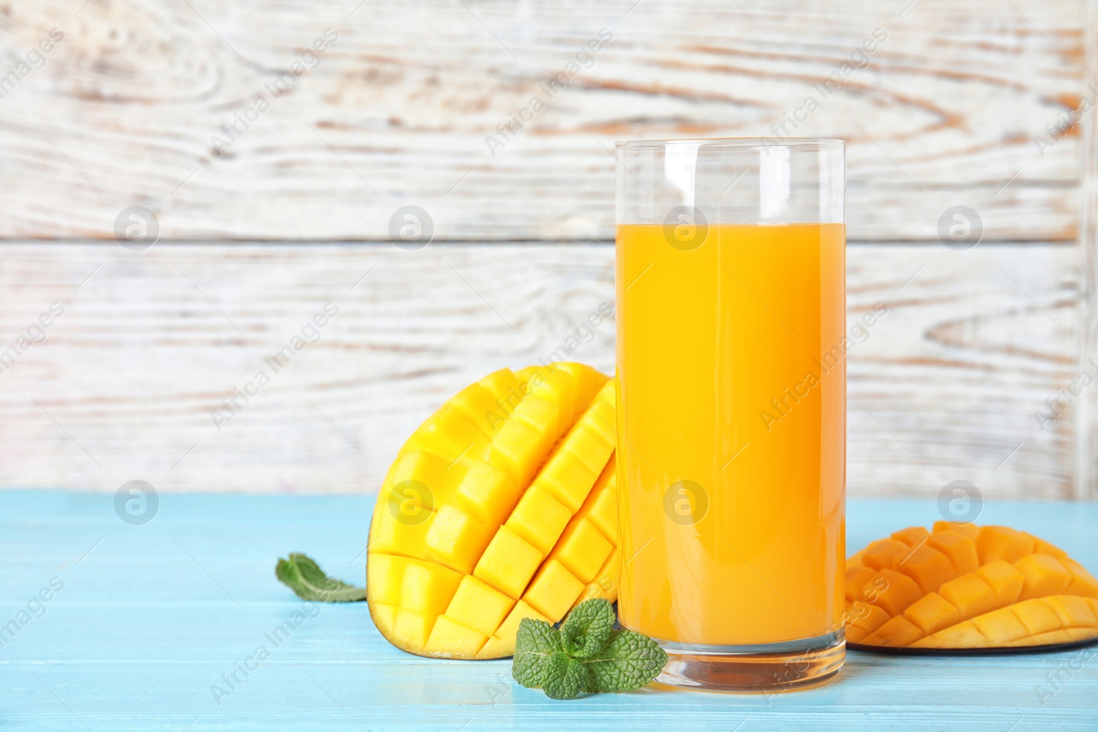 Photo of Glass with fresh mango juice and tasty fruits on wooden table. Space for text