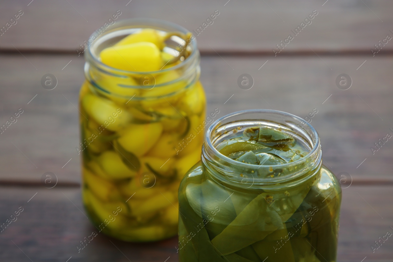 Photo of Glass jars of pickled green and yellow jalapeno peppers on wooden table, closeup