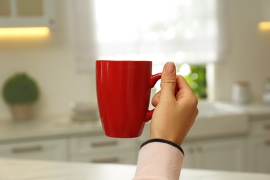 Woman holding elegant red cup in kitchen, closeup