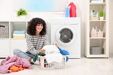 Photo of Happy woman with laundry near washing machine indoors