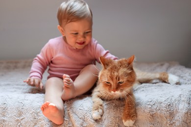 Photo of Adorable baby and cute red cat on bed indoors