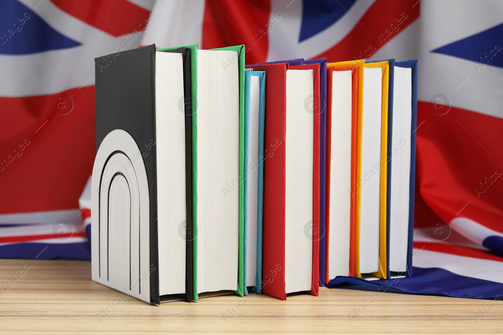 Photo of Learning foreign language. Different books on wooden table near flag of United Kingdom