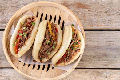 Photo of Delicious gua bao in bamboo steamer on wooden table, top view. Space for text
