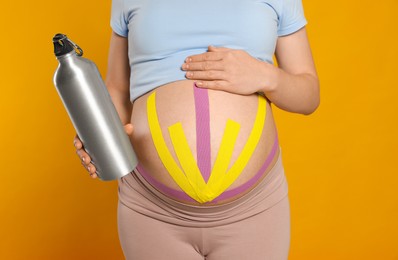 Photo of Pregnant woman with kinesio tapes holding water bottle on orange background, closeup