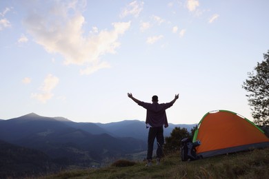 Tourist with backpack and sleeping pad near camping tent in mountains