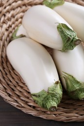 Photo of Fresh white eggplants in wicker basket on wooden table, closeup