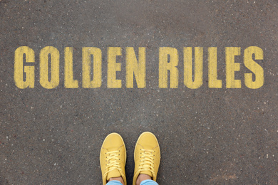 Woman standing near phrase GOLDEN RULES on asphalt, top view