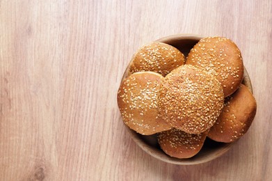 Photo of Bowl of fresh buns with sesame seeds on wooden table, top view. Space for text