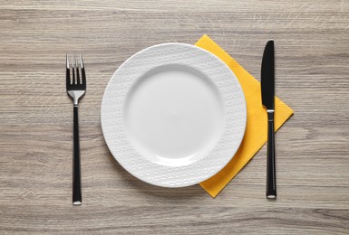 Photo of Plate with shiny silver fork and knife on wooden table, flat lay