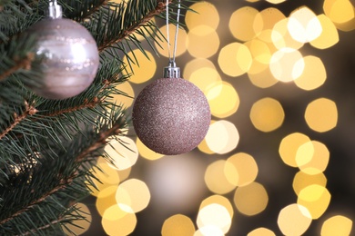 Photo of Shiny pink balls hanging on Christmas tree against festive lights, closeup