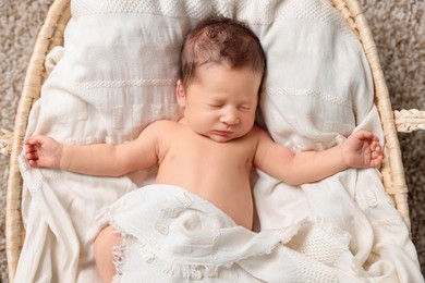 Cute newborn baby sleeping on white blanket in wicker crib, top view