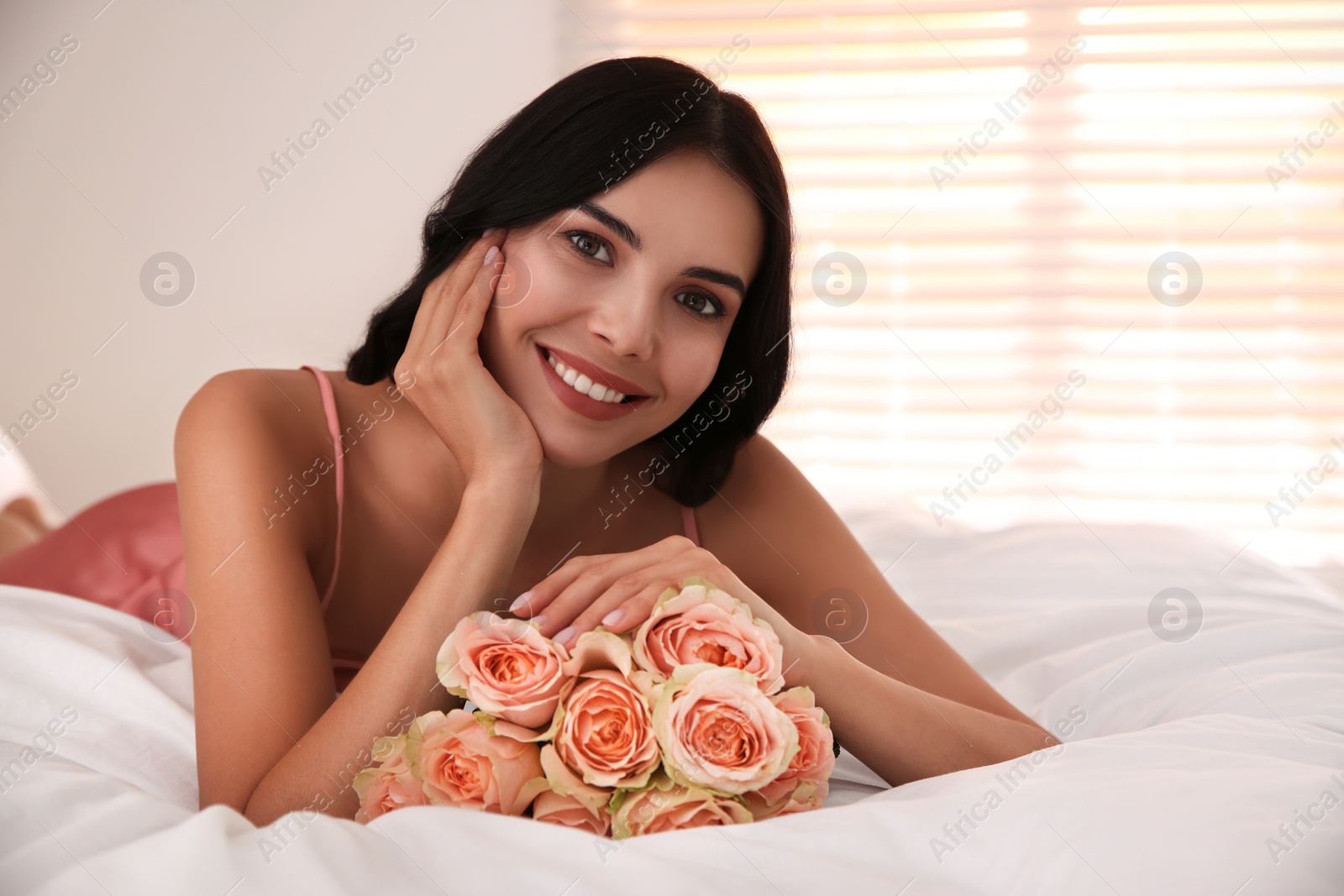 Photo of Young woman with beautiful bouquet on bed at home