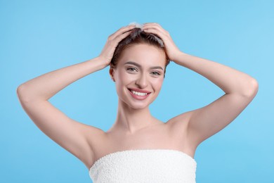 Photo of Happy young woman washing her hair with shampoo on light blue background