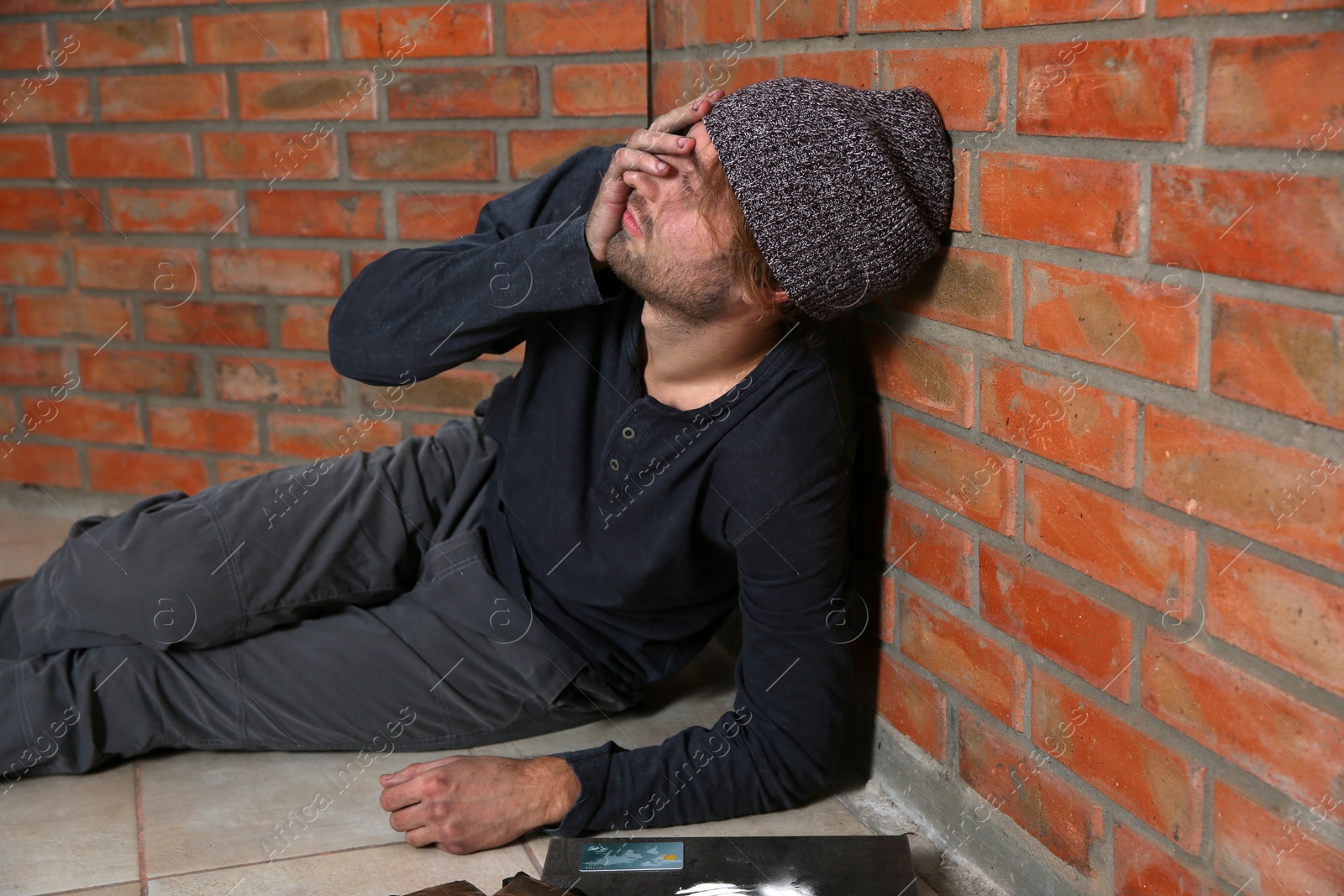 Photo of Young addicted man sitting near brick wall after using drugs