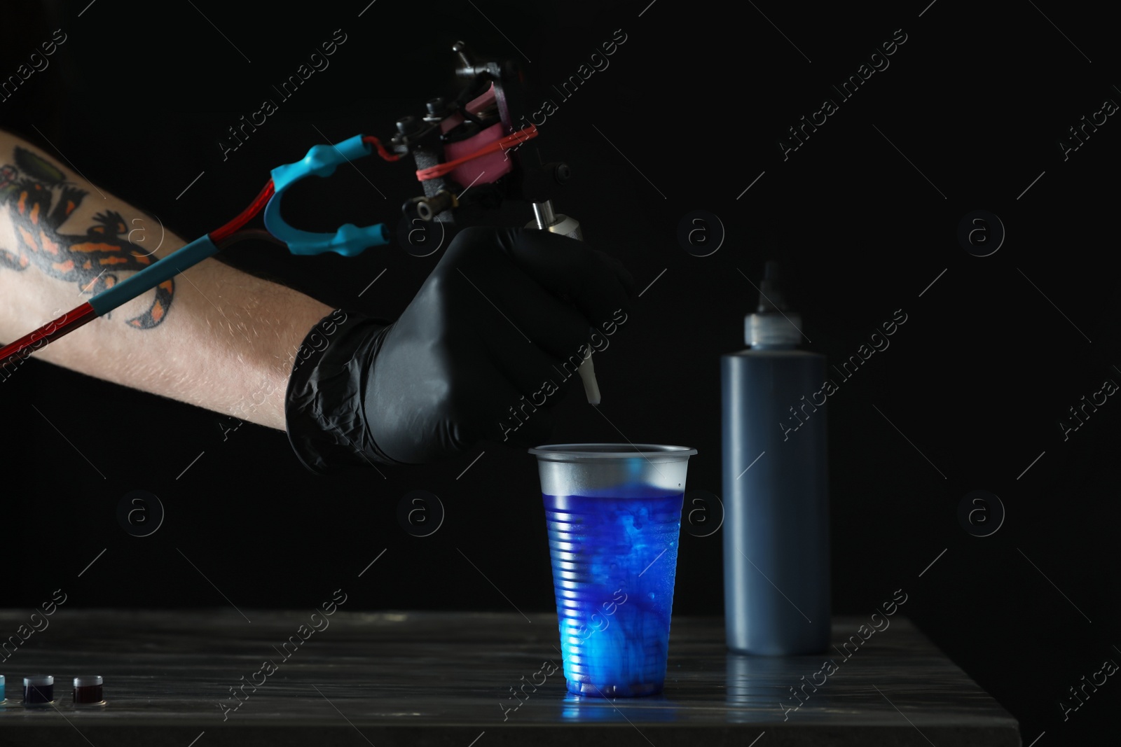 Photo of Tattoo artist cleaning machine needle at table, closeup