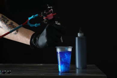 Tattoo artist cleaning machine needle at table, closeup