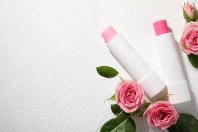 Photo of Lip balms and rose flowers on white textured background, flat lay. Space for text