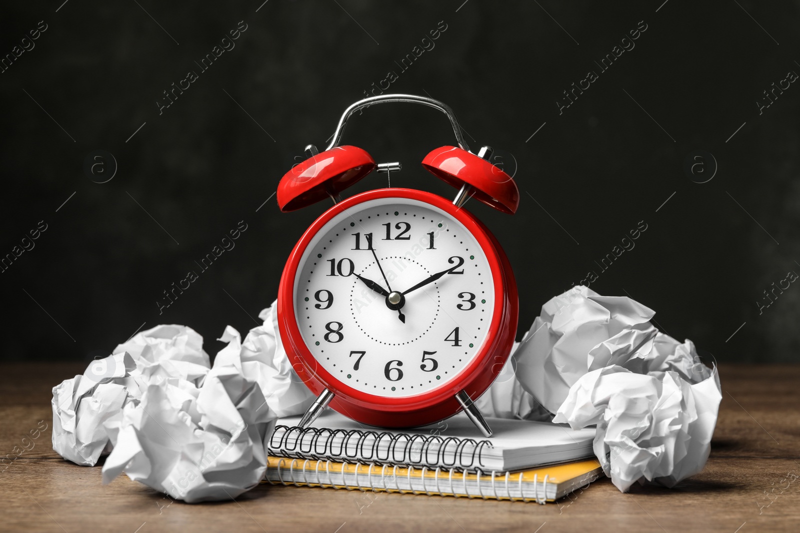 Photo of Crumpled paper balls, notebooks and alarm clock on wooden table