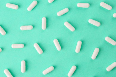 Photo of Vitamin capsules on turquoise background, flat lay
