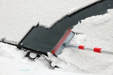 Photo of Cleaning car windshield from snow with squeegee, closeup