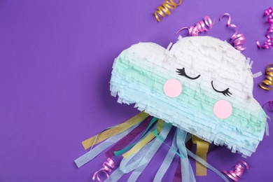 Cloud shaped pinata and streamers on purple background, flat lay. space for text